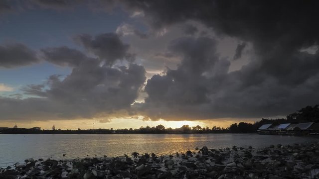 Time lapse evening of dark clouds moving above the lake with sunset and rain storm in cloudy sky background, Krajub reservoir, Nonk Kop in Ban Pong District, Ratchaburi, Thailand.