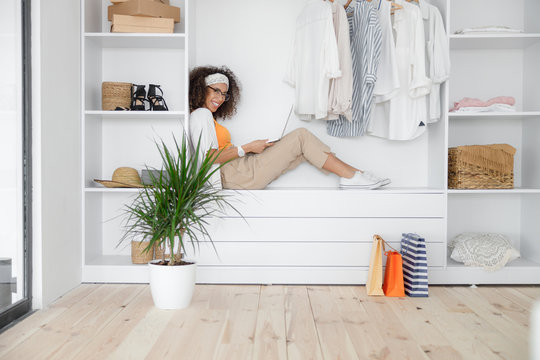 Cheerful Young Woman With Laptop Sitting In Closet