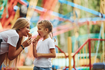 Eating ice cream. Cheerful little girl her mother have a good time in the park together near...