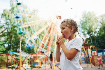 Cute little girl eats ice cream in the park at daytime near attractions