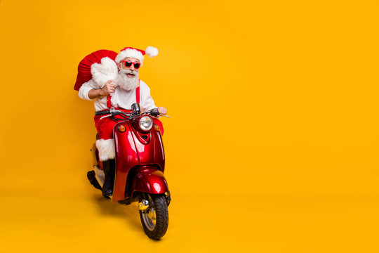 Full body photo of crazy funny santa claus in red hat drive hurry fast motor cycle hold sack christmas x-mas preparation ride north-pole wear shirt suspenders isolated yellow color background