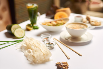 Colorful still life from food and vegetables prepared on white tablecloth. Tasty dinner from cream soup, tempura shrimps and salad waiting for guests. Rice noodles and herbal tea added to main meal.