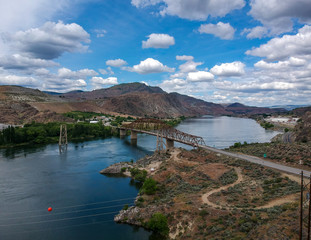 Great Aerial Photography of Beebe Bridge with a painfully blue sky and bright cumulus clouds in a craggy mountain setting with the Columbia River outside Chelan Washington