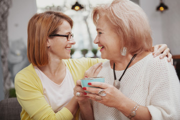 Close up of a mid aged woman hugging her senior mother, talking joyfully at the cafe