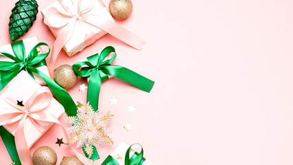 Pink Christmas card or New Year background, flat lay, copy space. Pastel pink gift boxes and green, golden decorations and ornaments border on pink desk, top view. Christmas shopping concept