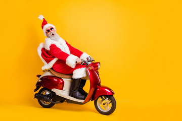 Full body photo of santa grandpa riding x-mas party by bike shocking moped speed wear stylish sun specs red coat trousers cap shirt boots isolated yellow color background © deagreez