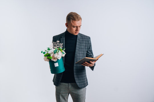 A young guy in the image of a teacher holds a box of flowers. Translation of the text on the wooden plate "Happy Teacher's Day."