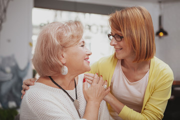 Mature woman smiling joyfully, hugging her senior mother at the coffee shop