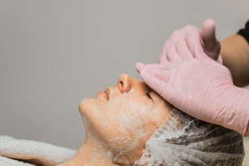 concept beautician. The hands of a cosmetologist put cream on the face of a woman. Beautician...