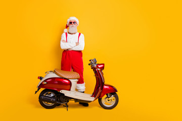 Fototapeta na wymiar Full body photo of santa man standing confidently near retro bike crossed arms not smiling wear trendy sun specs pants cap shirt isolated yellow color background