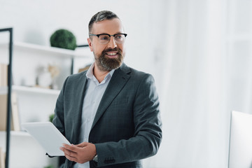 Fototapeta premium handsome businessman in formal wear and glasses using digital tablet in office
