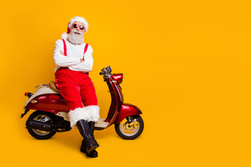 Full body photo of santa man festive mood ready x-mas theme party sitting retro bike listening jokes wear sun specs pants cap shirt boots isolated yellow color background