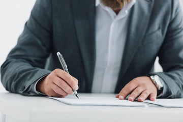 cropped view of businessman in formal wear writing with pen in office