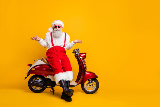 Full size photo of santa sit moped shrug shoulders not feel guilty coming party without gift wear specs suspenders pants cap shirt boots isolated yellow color background