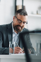 handsome businessman in formal wear and glasses writing with pen in office
