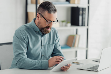 handsome businessman in shirt and glasses using digital tablet in office