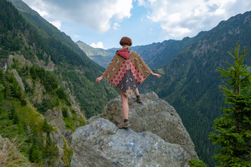 Young female traveler dressed in a poncho stand in the beautiful mountains 