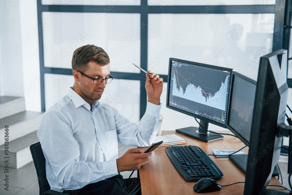 Poster using smartphone. young businessman in formal clothes is in office with multiple screens. conception