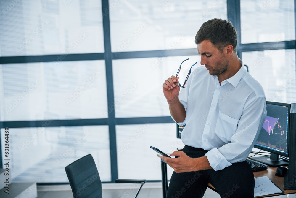 Poster sits on the table and having a break. with smartphone in hands. young businessman in formal clothes 