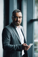 handsome businessman in formal wear and glasses holding smartphone