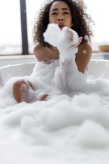 Charming young woman playing with foam in bath