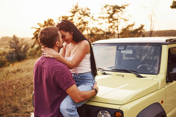 Lovely couple kissing outdoors. Girl sits on green jeep. Beautiful sunny evening