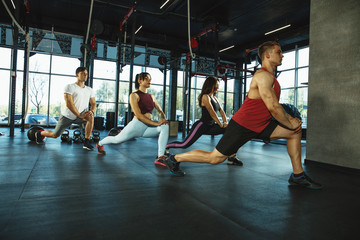 A group of muscular athletes doing workout at the gym. Gymnastics, training, fitness workout flexibility. Active and healthy lifestyle, youth, bodybuilding. Training in lunges and stretching exercises