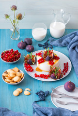 No bake cheesecake with salt caramel glaze embellished with fresh currant and figs with twigs of real rosemary herbs. Blue wooden table background.