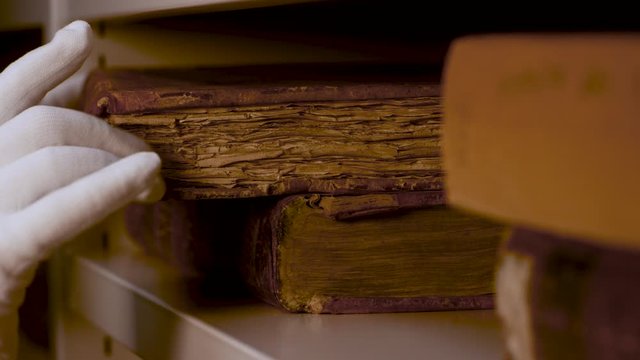 Close up of hands in white gloves putting on a shelve an old antique book very carefully. Stock footage. Ancient book with yellow pages in the storage.