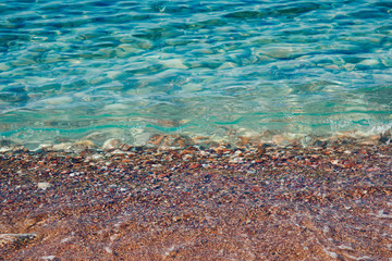 Turquoise sea waves splashing on pebble shore
