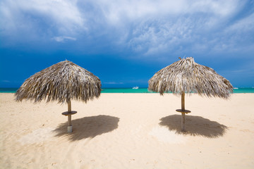 Palm tree leaves umbrellas on the beach against turquoise water of sea and dark cloudy sky, Punta Cana, Dominican Republic