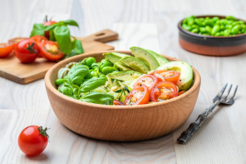 A fresh healthy salad with zoodles zucchini noodles, cherry tomatoes, avocado and edamame beans and fresh basil.