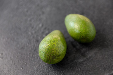 food, eating and vegetable concept - close up of two avocados on wet slate stone background