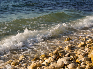 The sea wave runs on the shore. Foam sea wave rolls on the shore, covered with small pebbles.