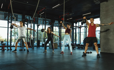 Fototapeta premium A group of muscular athletes doing workout at the gym. Gymnastics, training, fitness workout flexibility. Active and healthy lifestyle, youth, bodybuilding. Training with weights, doing squats.