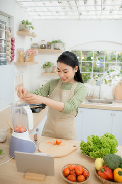 Image of young lady standing in kitchen using tablet computer and cooking vegetable salad