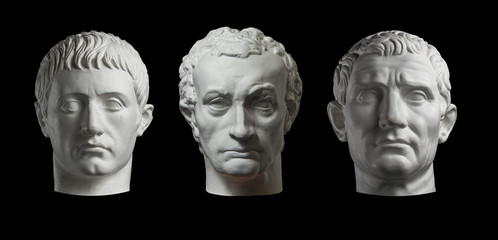 Three gypsum copy of ancient statue heads isolated on a black background. Plaster sculpture mans faces. - obrazy, fototapety, plakaty