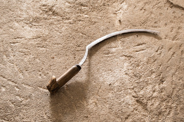 Old reaper sickle on rustic background