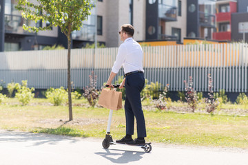 business and people and concept - young businessman with takeaway paper bag riding electric scooter outdoors