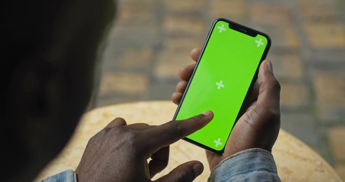 Close Up Shot of Head and Hand of Afro American Man Holding his Smartphone with Green Screen and Looking on it and Touching Screen. Backside View. Mock up.