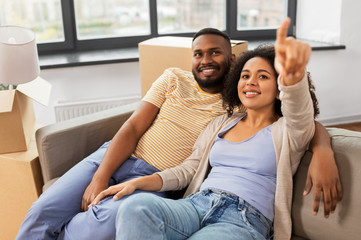 moving, people, repair and real estate concept - happy african american couple with cardboard boxes sitting on sofa at new home