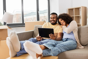 Fototapeta na wymiar mortgage, people and real estate concept - happy african american couple with tablet pc computer sitting on sofa at new home