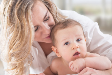 Mother and baby boy son playing on a white bed. Mothers tenderness and kisses of a toddler child