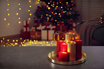 Lofty apartment with bunch of red and golden candles burning on stone table, traditional decorated christmas pine tree, bokeh lights on background. Close up, copy space.