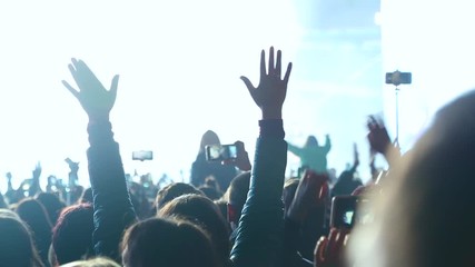 Crowd of spectators raises their hands up and applauds the musician performing on stage. Spectators at the concert photographed artist. Big crowd at concert cheering clapping hands at night concert.