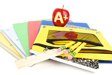 A plus grade carved into a red apple sitting on notebooks and school supplies