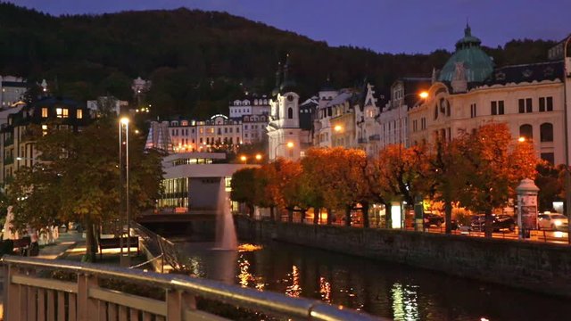 View from the bridge of illuminated buildings on embankments of Karlovy Vary in autumn evening, Czech Republic