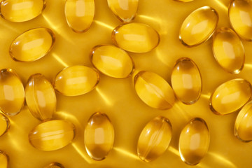 top view of golden shiny fish oil capsules scattered on yellow bright background