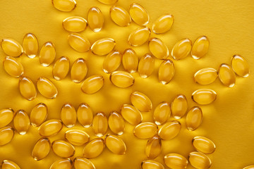 top view of golden shiny fish oil capsules scattered on yellow bright background