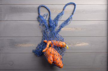 Ugly carrots concept in eco-friendly string bag on wooden background. Copy space